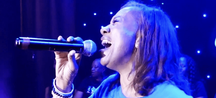 Person singing passionately on stage with microphone.